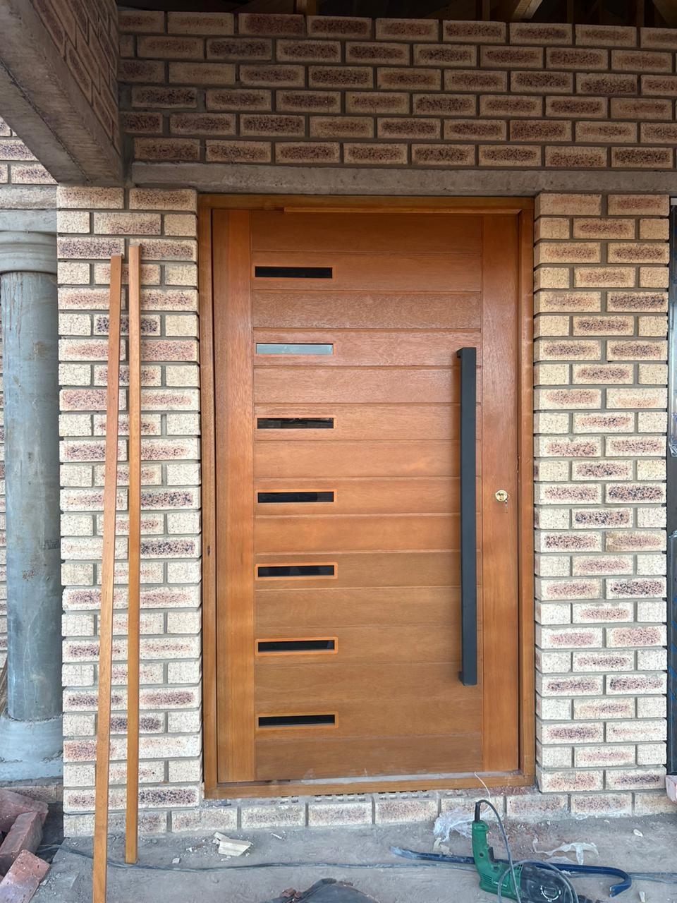 Solid meranti entrance door with slot vents on a new-build brick wall